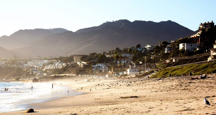 Coastal beach scene with hills and houses.