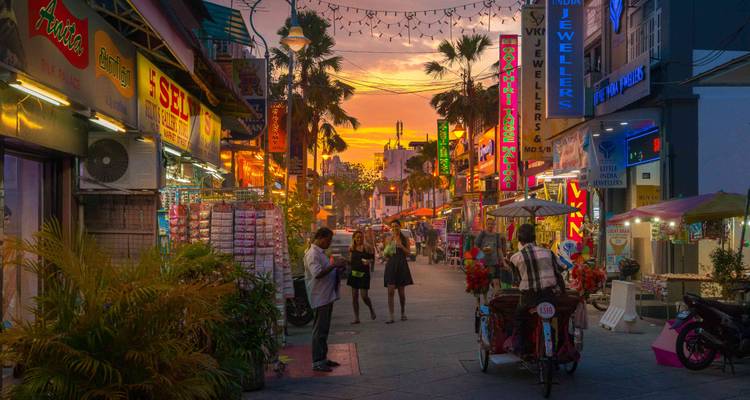 Mercado callejero bullicioso bajo una puesta de sol vibrante con palmeras.