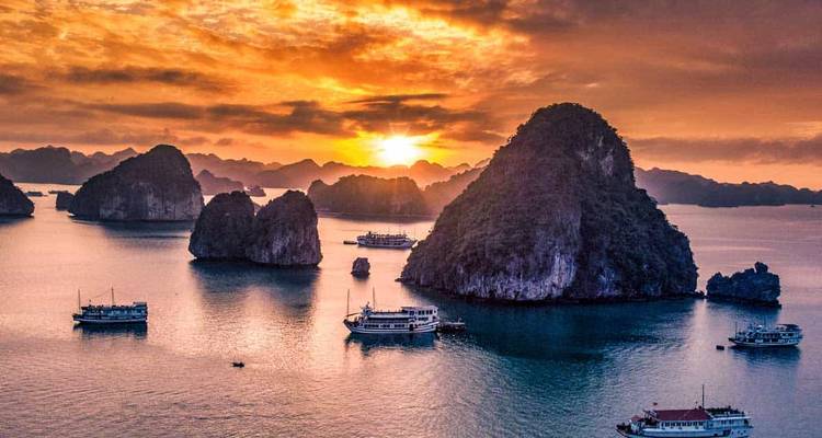 Majestic sunset over a bay with numerous boats and limestone formations.