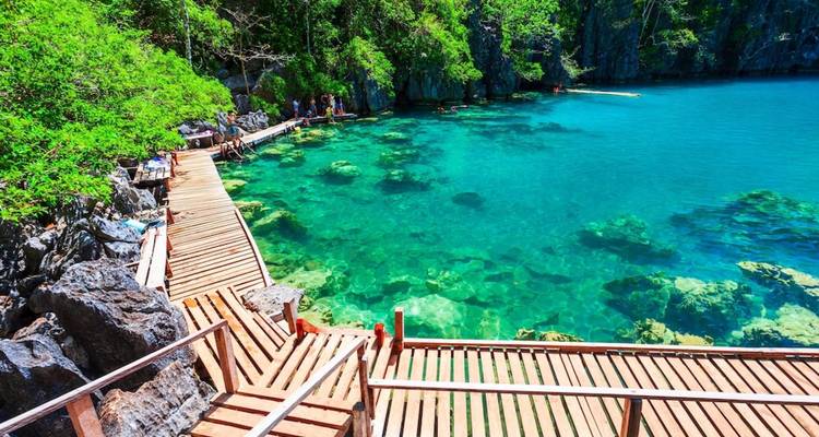 Passerelle en bois menant à une zone de baignade avec une eau claire dans un cadre tropical.