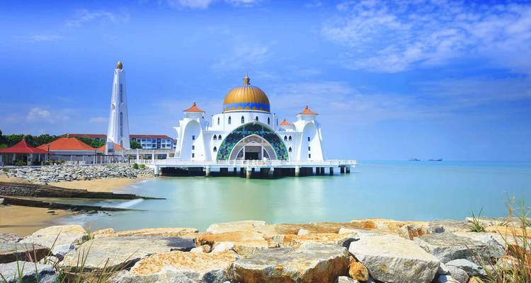 Elegant white Malacca Straits Mosque with golden dome extending over calm turquoise waters under a bright blue sky.