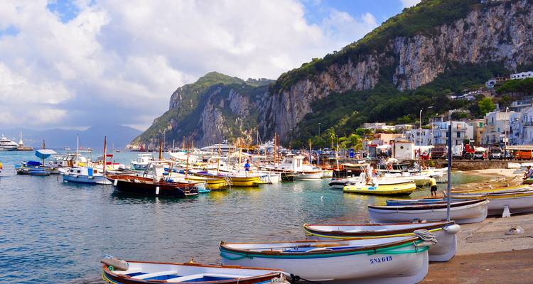 Colorful fishing boats moored in the picturesque harbor of Capri with towering cliffs behind.