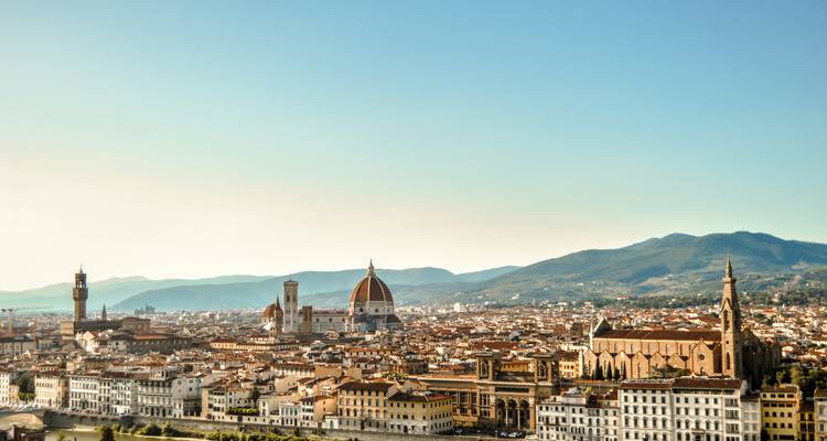 Expansive skyline of Florence with the Duomo and Palazzo Vecchio rising above terracotta rooftops at golden light.