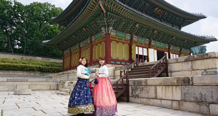 Deux femmes en hanbok coréen traditionnel posant devant un palais.