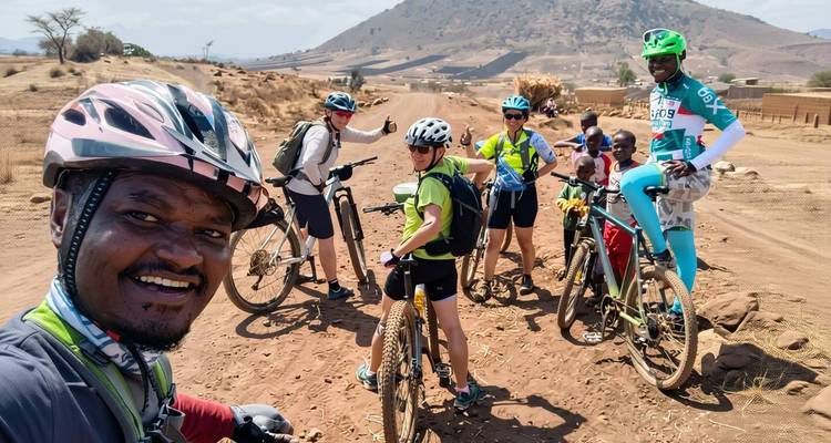 Groepsselfie van mountainbikers die poseren op een stoffig pad met een droog landschap en heuvels in de verte.