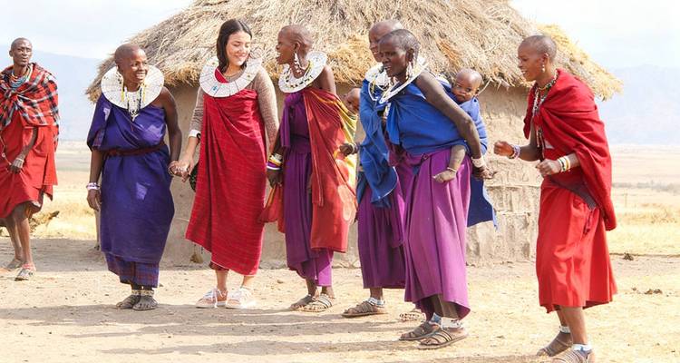 Plaatselijke Maasai dorpelingen in kleurrijke gewaden die dansen en contact maken met een bezoeker buiten een rieten hut.