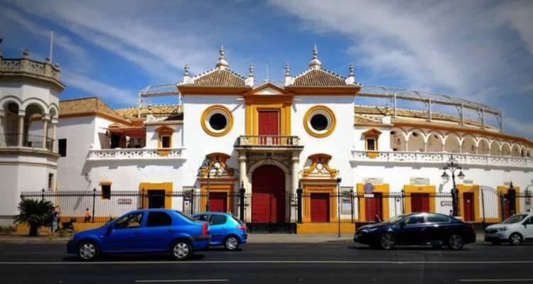 Die Außenansicht einer traditionellen Stierkampfarena mit charakteristischer Architektur und darum geparkten Autos.