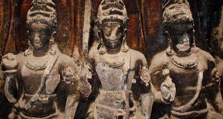 Trois anciennes statues de pierre aux traits usés dans un décor de grotte.
