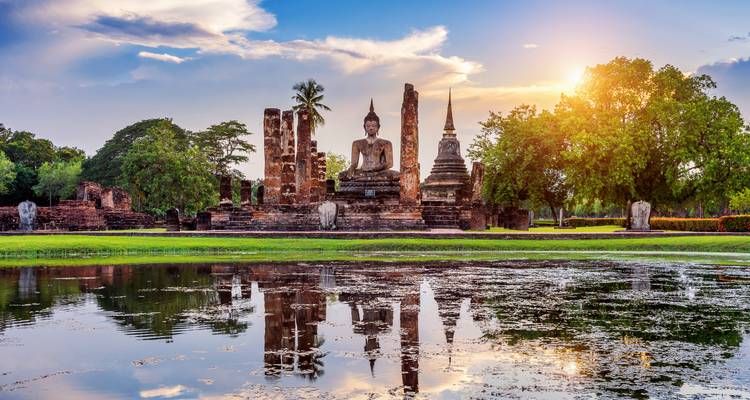 Ruinas históricas con una estatua de Buda y árboles con un reflejo en el agua.