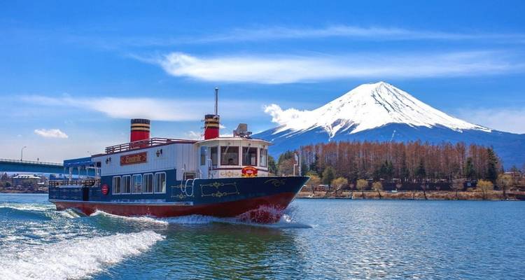 Kleurrijke rondvaartboot die over een meer vaart met de majestueuze Mount Fuji bedekt met sneeuw op de achtergrond.