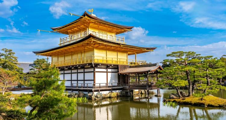 Het gouden Kinkaku-ji paviljoen weerspiegeld in de omringende vijver op een dag met een heldere blauwe lucht.