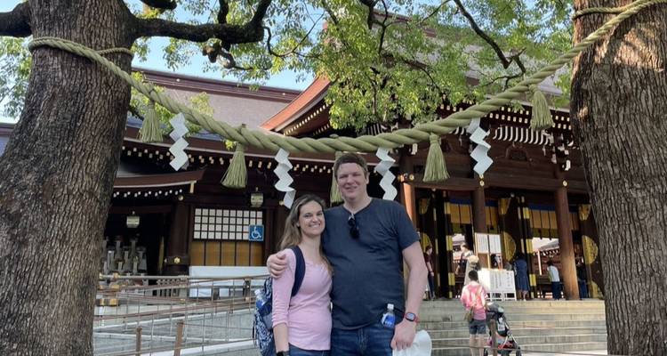 Glimlachend paar poseert onder heilige touwen op een traditionele Shinto heiligdom binnenplaats.