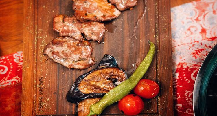 Planche en bois servant des tranches de viande grillée, aubergine, poivron vert et tomates à la mode azerbaïdjanaise.