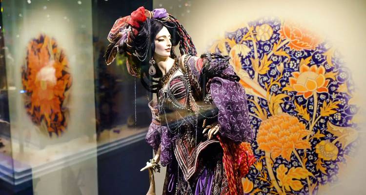 Mannequin théâtral orné en costume vibrant exposé dans un musée avec un arrière-plan en céramique décorative.