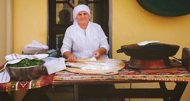 Femme locale préparant la pâte à pain plat près d'une plaque chauffante traditionnelle à un stand extérieur.
