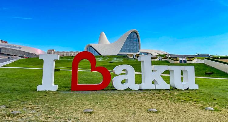 Grande pancarte « J'❤ Bakou » sur pelouse verte avec les courbes élégantes du Centre Heydar Aliyev en arrière-plan.