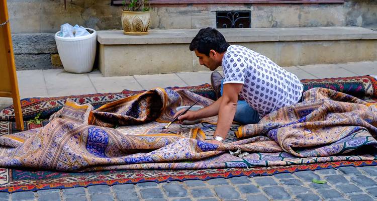 Artisan agenouillé sur des pavés restaurant un tapis à motifs dans le quartier historique de Bakou.