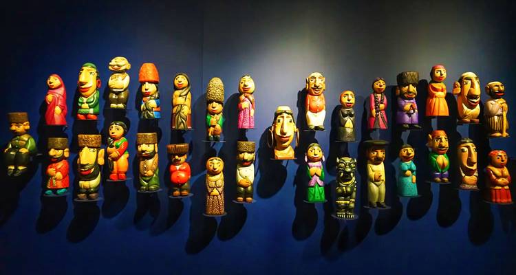 Mur d'exposition avec des rangées de figurines folkloriques peintes de couleurs vives montées sur un fond bleu foncé.