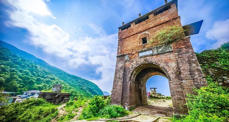 Historic stone gate in a lush landscape with mountains in the background.