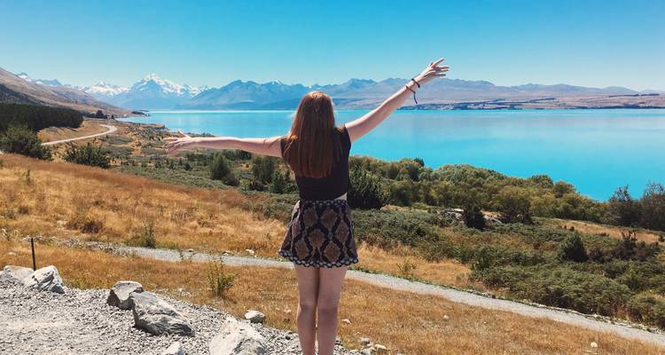 Woman with arms raised facing a beautiful lake and mountains.