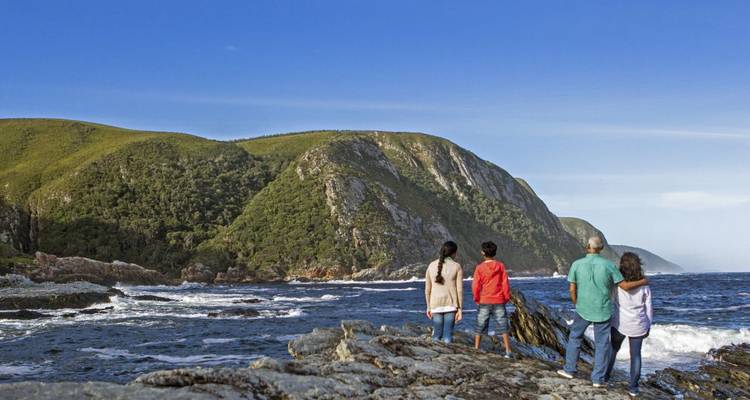 Eine Familie, die vom Meer von einer felsigen Küste mit grünen Hügeln blickt.