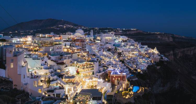 Santorini at night with lights illuminating the hillside buildings.