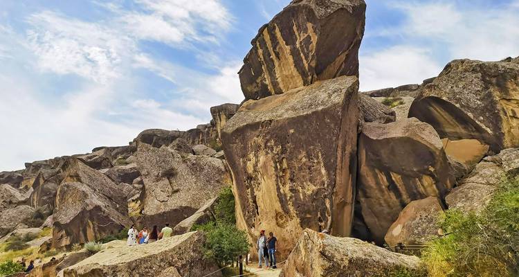 Riesige verwitterte Sandsteinblöcke und raue Landschaft von Gobustan mit Besuchern, die entlang eines Pfades wandern.