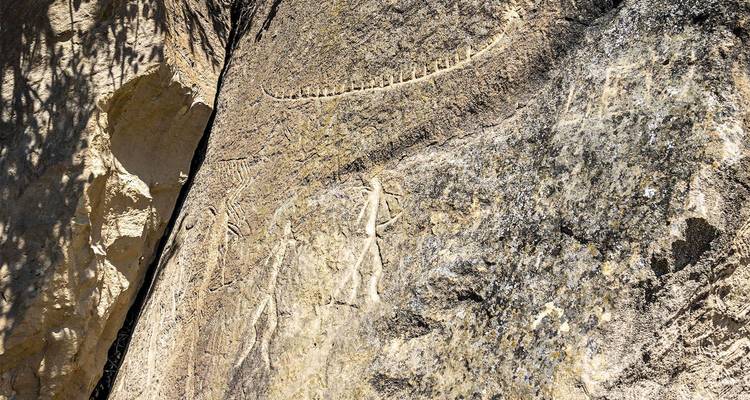 Nahaufnahme von antiken Petroglyphen-Gravuren auf einer sonnenbeschienenen Felswand.