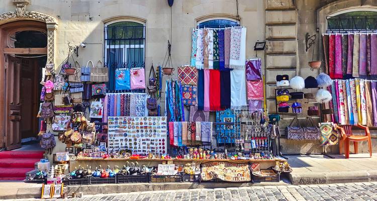 Straßenstand mit bunten Schals, Magneten und Kunsthandwerk vor einer Steingebäudemauer.