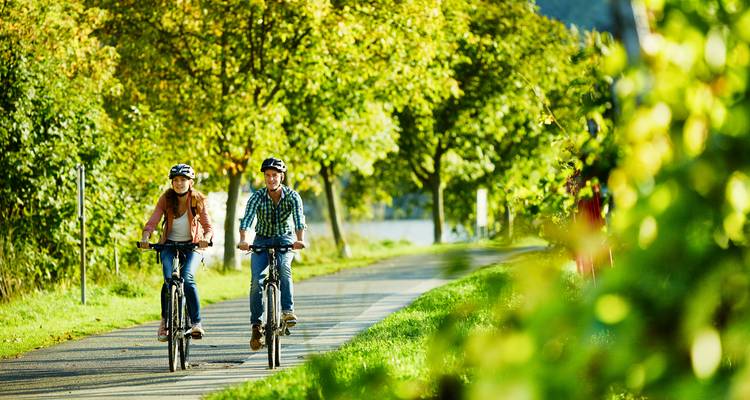 Deux jeunes cyclistes roulent le long d'une piste cyclable bordée de végétation en bord de rivière par une belle journée d'été.