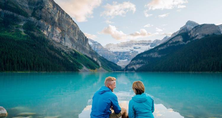 Pareja sentada junto a un lago azul cristalino con montañas.