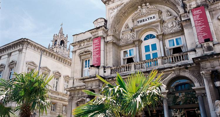 Façade de théâtre historique ornée avec des fenêtres bleues et des frondes de palmier sous un ciel dégagé.