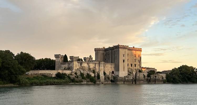 Forteresse médiévale au bord de la rivière illuminée par la douce lumière du coucher de soleil, reflétée dans une eau calme.