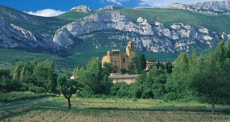 Monastère en pierre situé dans une vallée verdoyante sous des montagnes rocheuses spectaculaires.