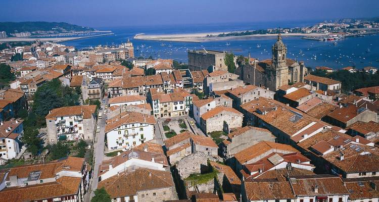 Vue aérienne des toits en tuiles rouges de Hondarribia à côté d'une estuaire scintillante.