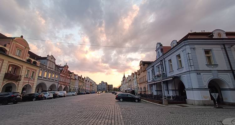 Ruhiger gepflasterter Platz, gesäumt von pastellfarbenen Barockgebäuden unter dramatischen Sonnenuntergangswolken.