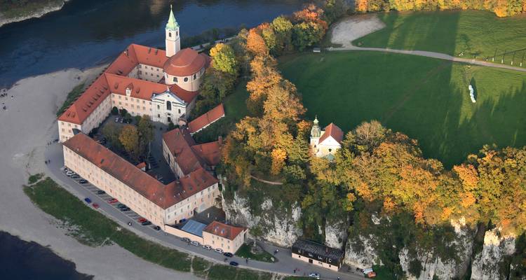 Luftaufnahme der Abtei Weltenburg auf einer Flussschleife, umgeben von Herbstwald.