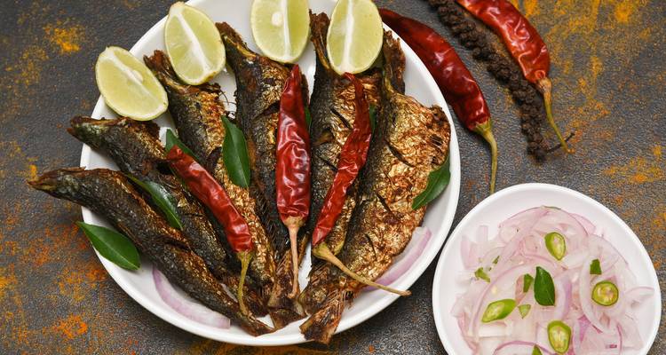 Teller mit gegartem Fisch, garniert mit Limette, Chilis und Zwiebeln.