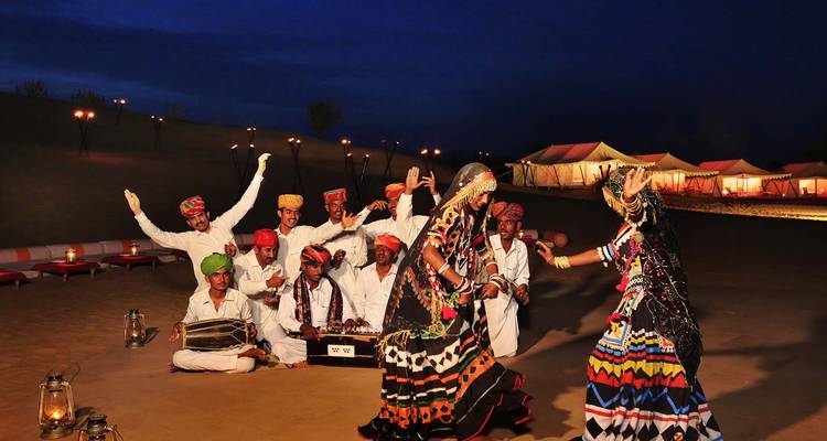 Traditionele Rajasthani artiesten die dansen in de woestijn, tenten op de achtergrond.