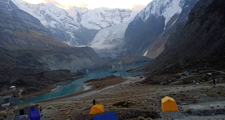 Lago glacial con montañas y tiendas de campaña, personas visibles.