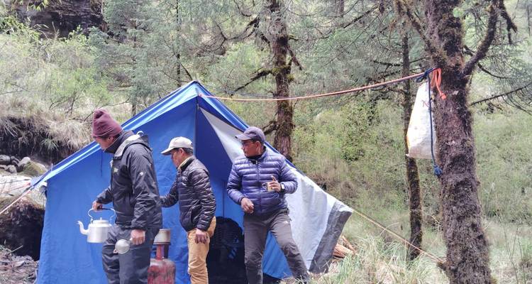 Tres individuos en un campamento con tienda de campaña y tetera.
