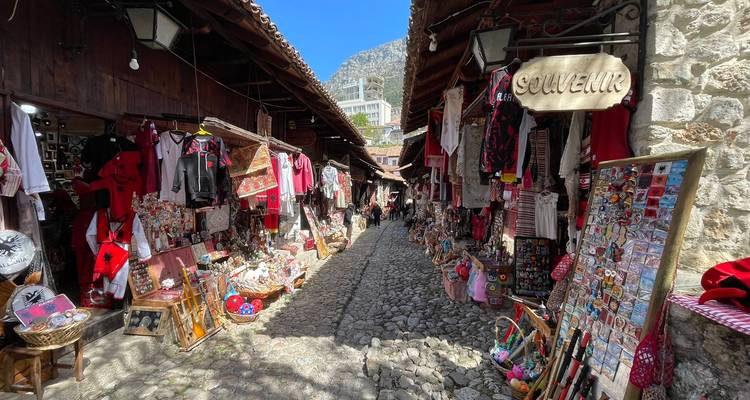 Bazar pavé étroit bordé d'étals de souvenirs colorés et de chalands sous un soleil éclatant.