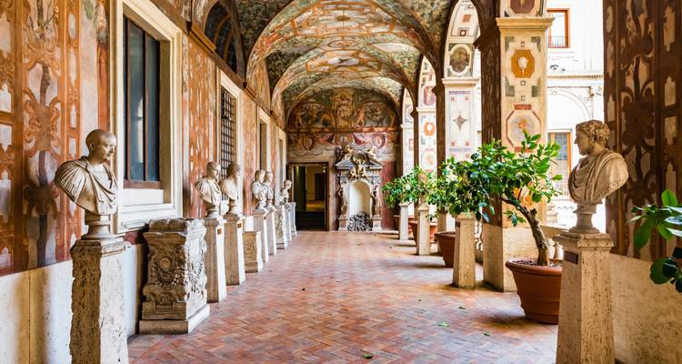 Élégant corridor de cloître Renaissance bordé de bustes en marbre, de plafonds ornés de fresques et d'agrumes en pot.