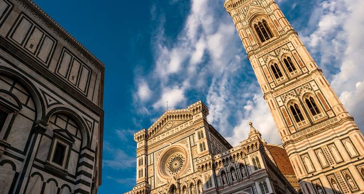 Vue en contre-plongée de la façade détaillée de la cathédrale de Florence et du campanile de Giotto sur un ciel bleu dramatique.