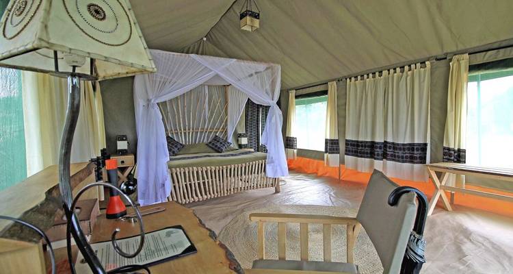 Innenraum eines Safari-Zeltes mit einem Bett und natürlicher Dekoration.