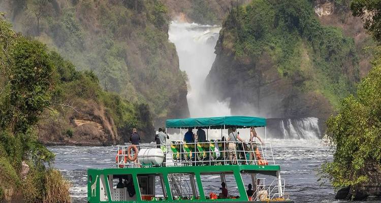 Bateau de tourisme rempli de visiteurs naviguant vers les puissantes chutes de Murchison qui se déversent en arrière-plan.