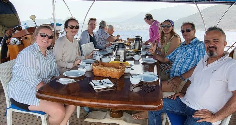 Groep mensen die genieten van een maaltijd op een bootdek met uitzicht op zee.