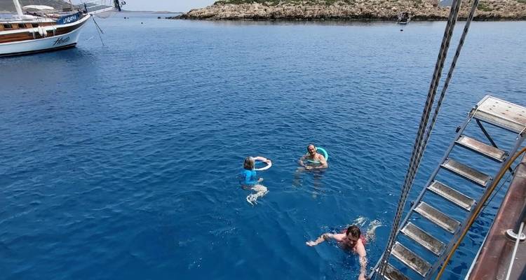 Drie mensen die zwemmen in helder blauw water bij een boot.