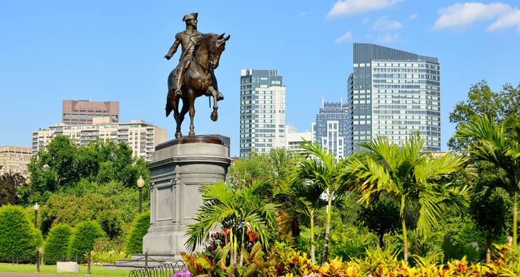 Statue d'un homme à cheval dans un parc urbain avec des bâtiments derrière.