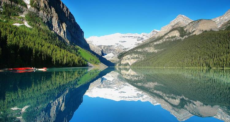 Le lac Louise, aux eaux parfaitement immobiles, reflète magnifiquement les montagnes Rocheuses enneigées et les forêts de pins denses.